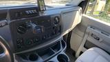 The interior dashboard of a 2013 Ford Econoline featuring control buttons a digital display and cup holders