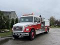 A 2001 Freightliner FL80 fire truck with a white cab and red accents features a shiny silver fire apparatus and flashing lights on top