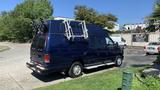 A 2013 Ford Econoline van in dark blue with a roof rack and ladder attached on the back