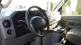 Interior view of a 2015 Ford Econoline showing the steering wheel dashboard and center console with controls and cup holders