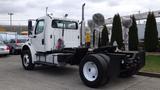 A 2003 Freightliner M2 106 truck featuring a white cabin with a flatbed chassis and visible drivetrain components