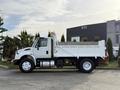 A 2015 International DuraStar 4300 dump truck shown in profile with a white body and a flatbed dump area raised slightly