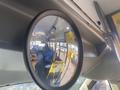 A convex mirror mounted on the ceiling of a bus reflecting the interior with blue seats and yellow handrails