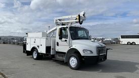 A white 2010 Freightliner M2 106 utility truck with a raised aerial lift and enclosed storage compartments on the side