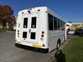 A white 2015 Chevrolet Express shuttle bus with large rear doors and reflective lights