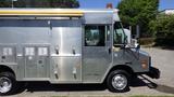 A 2005 Morgan Olson Workhorse delivery truck with a shiny aluminum exterior featuring multiple compartments and a yellow roof light