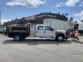 A 2010 Ford F-550 with a snow plow attached in front and a flatbed truck body with storage compartments on the side