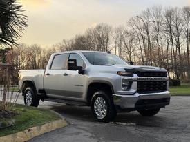 A 2023 Chevrolet Silverado 3500HD in silver with chrome accents parked on a driveway showcasing its large wheels and bold front grille