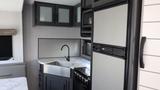 A modern kitchen interior of a 2022 Aspen Trail trailer featuring a stainless steel sink a black faucet a stove and a refrigerator with a sleek design