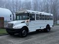 A white 2016 International 4200 bus with multiple windows and a yellow light bar on top parked on a concrete surface