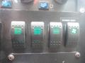 Four black control switches with green indicators labeled power vent, heater, and a fan symbol on a dashboard panel