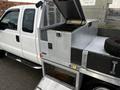 A white 2014 Ford F-250 SD with an open tool box in the truck bed and a spare tire resting on the side of the truck