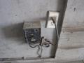 A weathered electrical box mounted on a wall with a power cord plugged into a single wall outlet