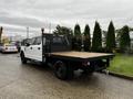 A white 2020 Ford F-350 SD with a flatbed truck bed and black accents parked on a street with greenery in the background