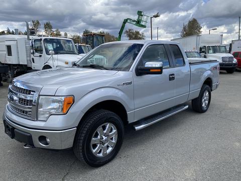 A silver 2013 Ford F-150 with a crew cab and chrome wheels parked with a truck bed cover and side steps