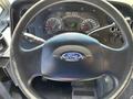 Close-up view of a 2012 Ford Econoline steering wheel featuring the Ford logo and dashboard gauges visible in the background