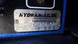 A metal identification plate displaying the text "HYDRAMASTER CORPORATION Mukilteo WA 98275" with a model number on a blue surface