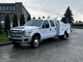 A white 2014 Ford F-350 SD with a utility bed and tools on the side parked on a street