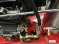 A close-up of the pump and engine components of a 2024 Magnum 4000 Hot Water Pressure Washer with hoses and a control valve in the foreground