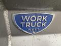 A badge displaying the words WORK TRUCK WEST on a metallic surface with raindrops on it