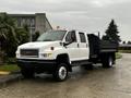 A white 2005 GMC C5 Duramax truck with a flatbed and orange warning lights parked on a roadway.