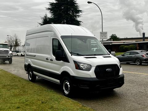 A white 2021 Ford Transit van with a high roof and black grille parked on a street with a wet surface