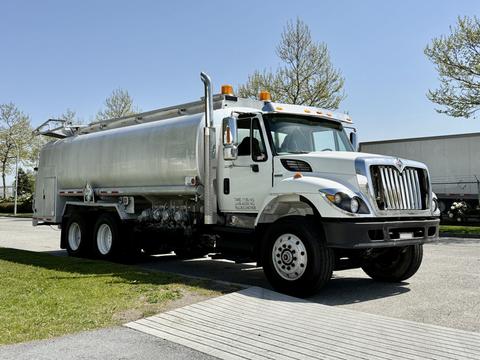 A 2009 International 7500 truck with a silver tank body and black wheels parked on a driveway