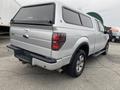 A silver 2014 Ford F-150 pickup truck with a camper shell on the bed parked at an angle showing the rear and side views