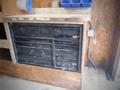 A black tool cabinet with multiple drawers, featuring a metal frame and a handle, mounted below a wooden countertop in a workshop setting