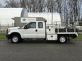 A white 2014 Ford F-250 SD with a utility bed and tool compartments on both sides is parked facing left