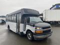 A 2018 Chevrolet Express bus in white with a black front grille and tinted windows parked at a location with slight rain visible on the windshield