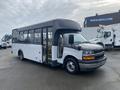 A 2017 Chevrolet Express shuttle bus with a white and black exterior and large side windows is parked with its doors open