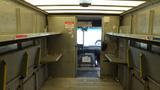 Interior view of a 2011 Ford Econoline showing empty shelves on both sides and a doorway leading to the driver's area