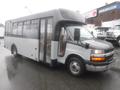 A 2016 Chevrolet Express shuttle bus with a black front and gray sides featuring large windows and a door on the side for passenger entry