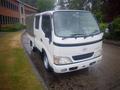 A 2003 Toyota Toyoace truck with a white body and a canvas cover on the back parked on a wet surface