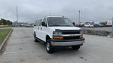 A 2017 Chevrolet Express Quigley 4x4 van parked in a vacant lot with a white exterior and a silver band on the front bumper