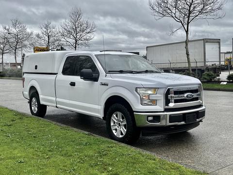 A 2017 Ford F-150 in white with a truck cap parked on a wet surface with its driver's side facing the viewer