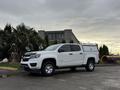 A white 2018 Chevrolet Colorado pickup truck with a gray canopy on the bed parked on a paved area