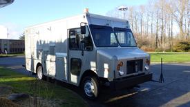 A silver 2008 Morgan Olson Workhorse delivery truck with a rectangular body and large windows parked on a street