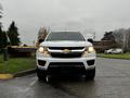 A white 2019 Chevrolet Colorado facing forward with its headlights on and a prominent front grille featuring the Chevrolet logo