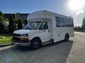 A white 2015 Chevrolet Express bus with large windows and a boxy shape is parked at an angle displaying its side and front view