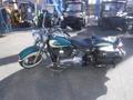 A 2009 Harley-Davidson FLSTC in teal and silver with a black leather seat and studded saddlebags parked on a flat surface