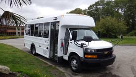 A 2023 Chevrolet Express bus parked with an open door and a single side mirror visible