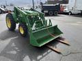 A green 2003 John Deere 790 tractor with a front loader attachment and wooden forks attached to the bucket