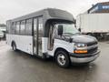 A 2017 Chevrolet Express bus with a white and gray exterior featuring large windows and a wheelchair-accessible entrance