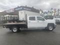 A white 2015 Chevrolet Silverado 3500HD with a flatbed in the foreground displaying chrome wheels and a crew cab configuration