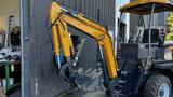 A yellow and black 2024 AGT BH50G backhoe loader with an articulated arm and bucket attachment positioned next to a wall