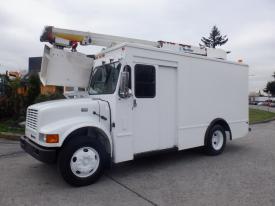 A white 2002 International 4700 truck with a raised bucket lift on top and large wheels parked on a paved surface