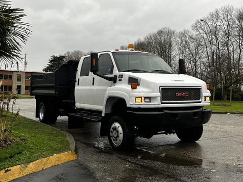 A white 2005 GMC C5 Duramax truck with a black flatbed and orange warning light on top parked at an angle