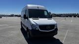 A 2016 Mercedes-Benz Sprinter van in white with a black front bumper parked in a lot facing the camera